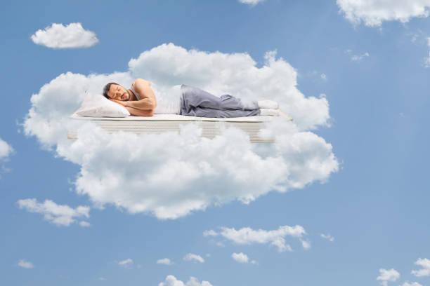 hombre en pijama durmiendo en un colchón y flotando en el cielo - colchones fotografías e imágenes de stock