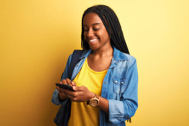 istock African american student woman using smartphone standing over isolated yellow background with a happy face standing and smiling with a confident smile showing teeth 1214255581
