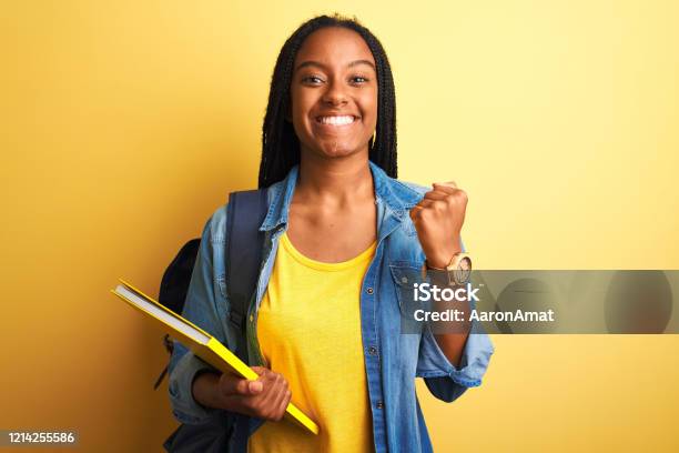 Mujer Estudiante Afroamericana Con Mochila Y Libro Sobre Fondo Amarillo Aislado Gritando Orgulloso Y Celebrando La Victoria Y El Éxito Muy Emocionado Animando La Emoción Foto de stock y más banco de imágenes de Estudiante