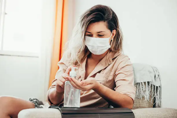 Photo of Coronavirus. Woman in quarantine wearing protective mask sanitizing her hands with alcohol gel