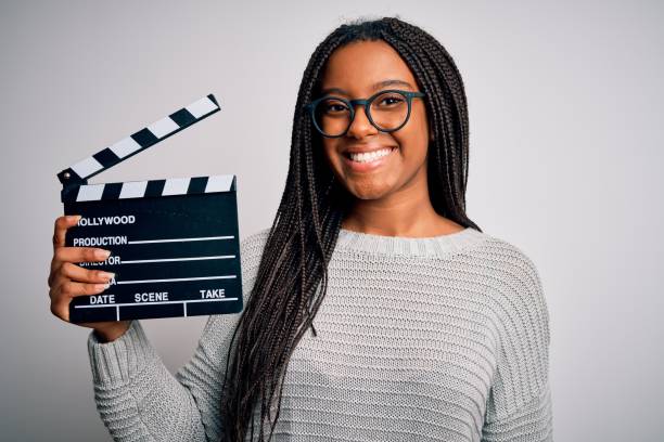 junge afrikanische amerikanische regisseur mädchen filmt einen film mit klatschbrett über isolierten hintergrund mit einem glücklichen gesicht stehen und lächelnd mit einem selbstbewussten lächeln zeigt zähne - filmregisseur stock-fotos und bilder