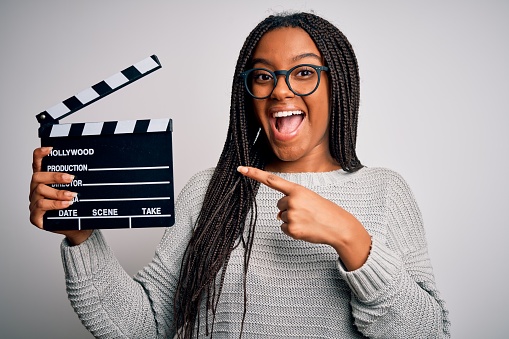 Young african american director girl filming a movie using clapboard over isolated background very happy pointing with hand and finger