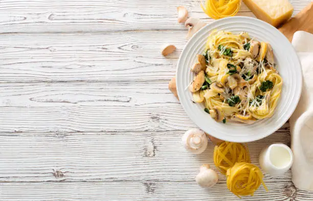 Italian pasta( fettuccini) with mushrooms, chicken meat, spinach, parmesan cheese and cream sauce on a white wooden background. Flat lay. Copy space