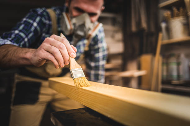 istock Carpenter with mask applies paint using paintbrush in carpentry workshop 1214260137