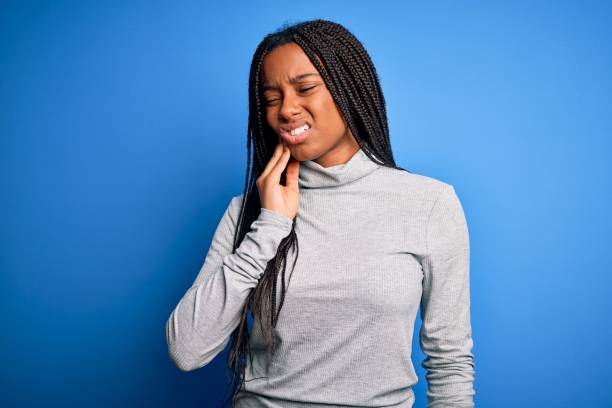 young african american woman standing wearing casual turtleneck over blue isolated background touching mouth with hand with painful expression because of toothache or dental illness on teeth. dentist - dentist pain human teeth toothache imagens e fotografias de stock