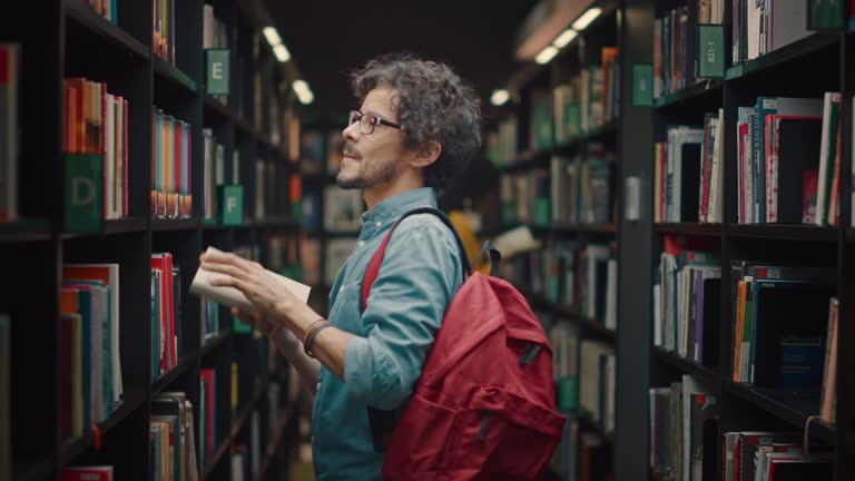 University Library: Portrait of Focused and Talented Hispanic Boy Wearing Glasses Picks Right Book Title From Bookshelf for His Class Assignment and Exam Preparations.Side View Portrait