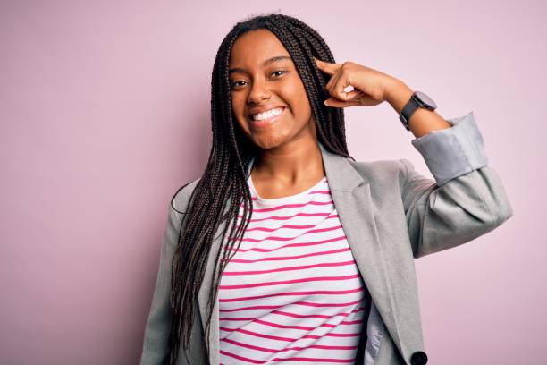 jeune femme d’affaires afro-américaine restant au-dessus du fond isolé rose souriant pointant à la tête avec un doigt, grande idée ou pensée, bonne mémoire - isolated on black young adult portrait business photos et images de collection