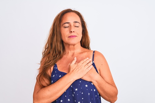 Middle age mature woman standing over white isolated background smiling with hands on chest with closed eyes and grateful gesture on face. Health concept.