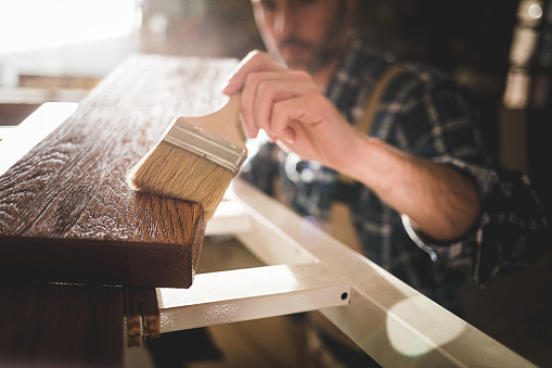 El primer plano del pincel aplica pintura o barniz en tablero de madera en el taller de carpintería photo