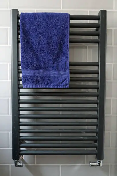 Modern contempoary gray gunmetal ladder radiator with a blue towel and grey tiles. New build house. Close up. Billericay, Essex, United Kingdom, March 21, 2020