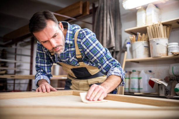 istock Professional carpenter polishing wood using abrasive paper in carpentry workshop 1214268446