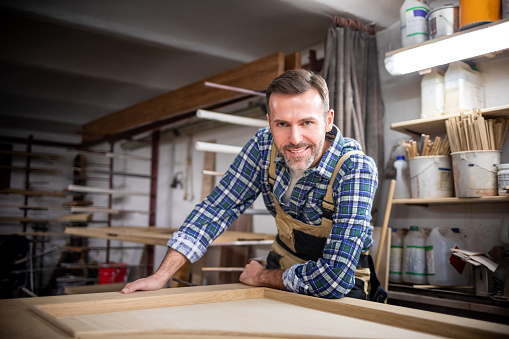 Smiling and proud mature carpenter in his carpentry workshop