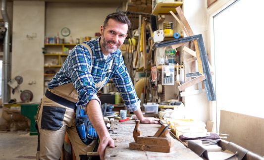 Smiling and proud mature carpenter in his carpentry workshop