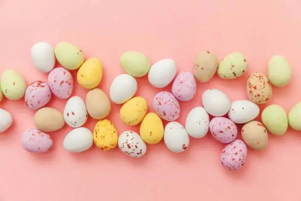Happy Easter concept. Preparation for holiday. Easter candy chocolate eggs and jellybean sweets isolated on trendy pastel pink background. Simple minimalism flat lay top view copy space