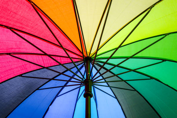 Multi-colored colorful umbrella with all colors of the rainbow in sunlight on a blue background. Bright texture background.