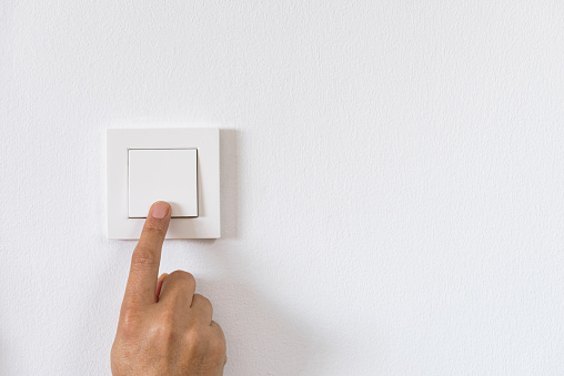 Cropped hand of man pressing switch board against wall.