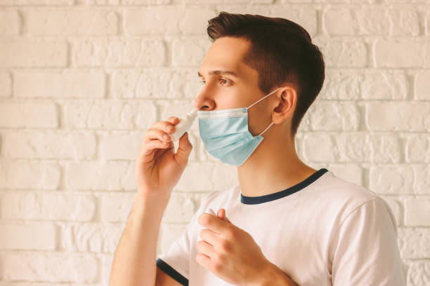 Sick young man using nose drops for congested nose Portrait of young sick man using nasal drops for runny congested nose. Confident sick doctor in medical protective mask on face using nose spray. Pandemic coronavirus COVID-19 nCov-19 symptoms nasal spray stock pictures, royalty-free photos & images