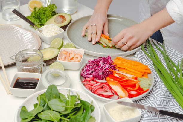 istock The process of cooking spring rolls - woman's hands putting rolling spring roll with basil, pepper and cucumber. Table with spring rolls ingredients, fresh vegetables, geen onion and avocado. 1214272989