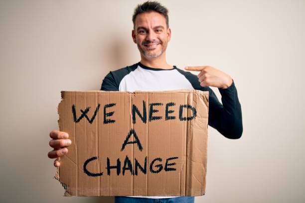 istock Young handsome activist man holding banner with change message over pink background with surprise face pointing finger to himself 1214274479
