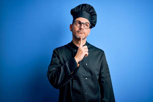 istock Young handsome chef man wearing cooker uniform and hat over isolated blue background Thinking concentrated about doubt with finger on chin and looking up wondering 1214275858