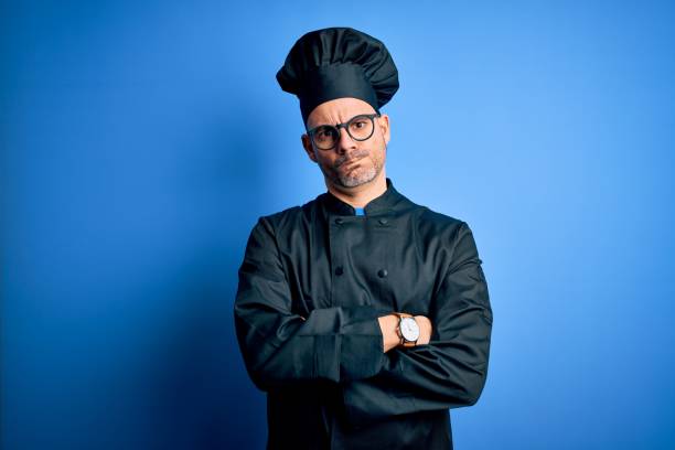 istock Young handsome chef man wearing cooker uniform and hat over isolated blue background skeptic and nervous, disapproving expression on face with crossed arms. Negative person. 1214275919