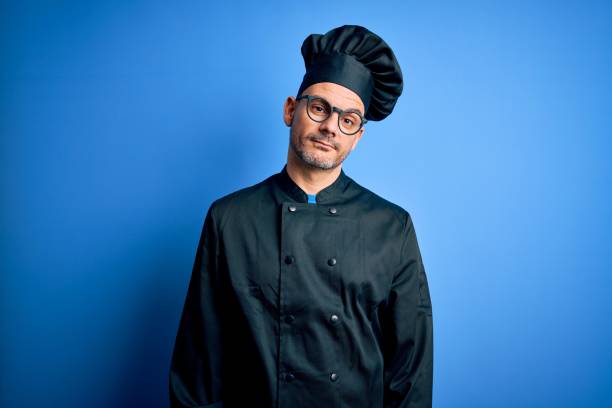 istock Young handsome chef man wearing cooker uniform and hat over isolated blue background looking sleepy and tired, exhausted for fatigue and hangover, lazy eyes in the morning. 1214275952