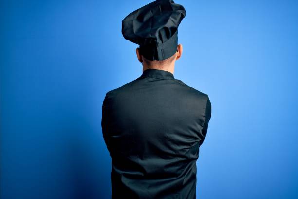 istock Young handsome chef man wearing cooker uniform and hat over isolated blue background standing backwards looking away with crossed arms 1214275969