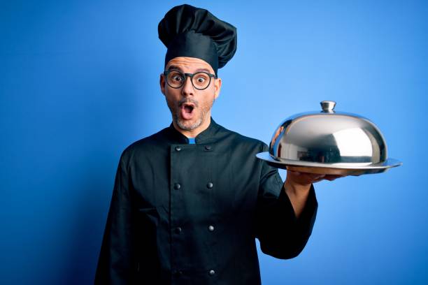 istock Young handsome chef man wearing uniform and hat holding waiter tray with dome scared in shock with a surprise face, afraid and excited with fear expression 1214276024