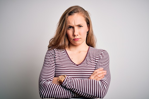 Young beautiful blonde woman wearing casual striped t-shirt over isolated white background skeptic and nervous, disapproving expression on face with crossed arms. Negative person.