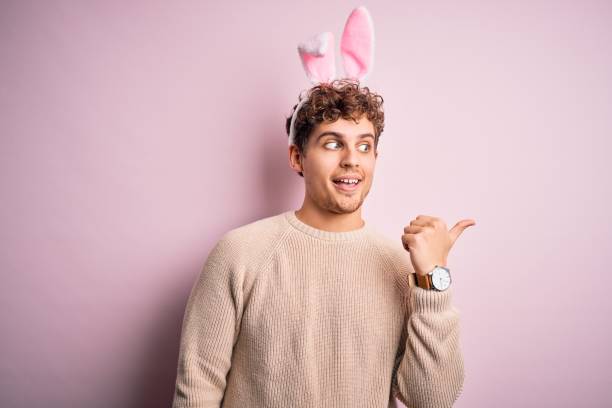 istock Young handsome blond man wearing easter rabbit ears over isolated pink background smiling with happy face looking and pointing to the side with thumb up. 1214281298