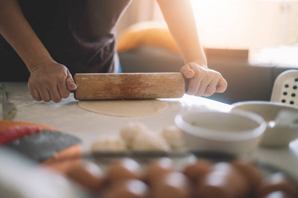 an asian chinese house wife preparing food using rolling pin with flour mixed with eggs on table making dough