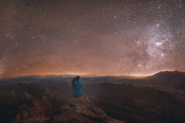 Silhouette of woman tourist with long hair feeling freedom and happiness looking at the night star sky and Milky Way above the Moon Valley canyon in Atacama desert, South America, Chile
