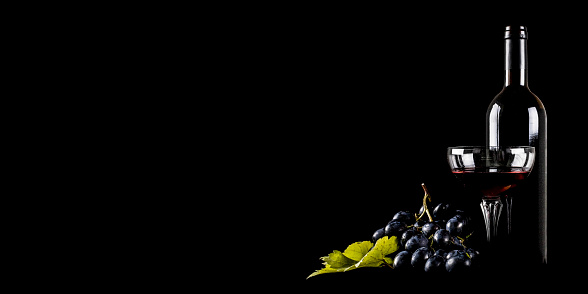 Bottle of red wine with a glass and grape on black background