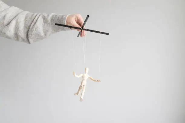 Photo of Human hand holds a wooden doll on the clothesline on a gray background with place for text. Power metaphor concept