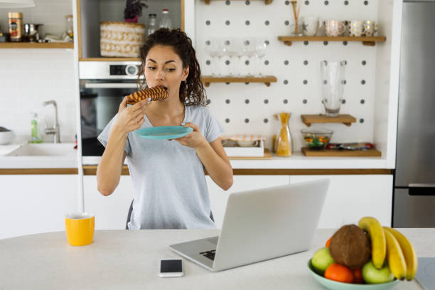 istock Young woman heaving breakfast in her kitchen, using laptop, browsing internet.. 1214297861