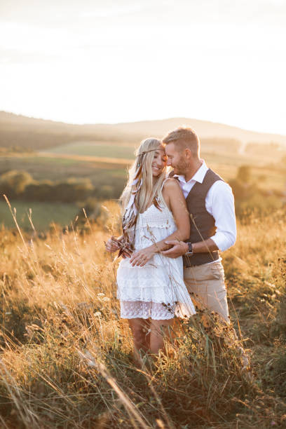 istock Young couple in stylish boho rustic clothes embracing, standing in the field at sunset. Boho love story, couple on a walk in the field 1214301168