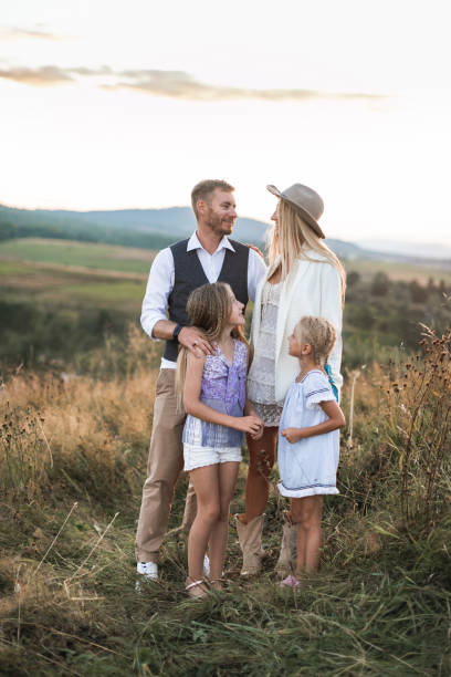 istock Young beautiful family posing and looking each other, while standing in a field, at summer sunset. Family relaxing in summer field. Family, love, vacation concept 1214301384
