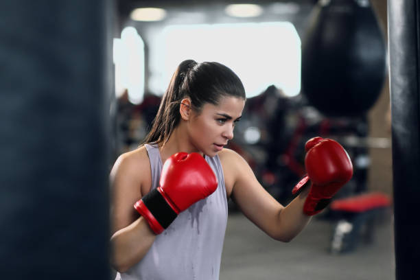 Athletic young brunette woman in sportswear and red boxing gloves trains bumps on a punching bag in a fitness gym. stock photo