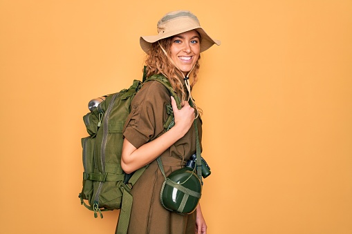 Young blonde explorer woman with blue eyes hiking wearing backpack and water canteen with a happy and cool smile on face. Lucky person.