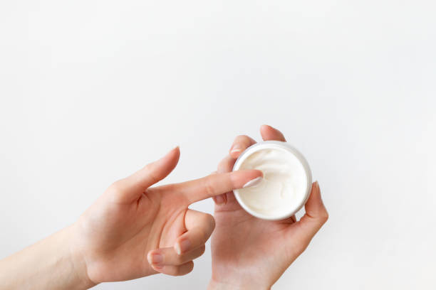 Girl finger applying moisturizer cream in white plastic container on white background. Daily routine skincare and bodycare, top view stock photo