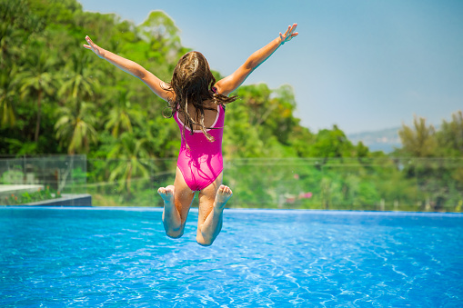Excited funny little girl jumping to the swimming pool. Happy summer vacation