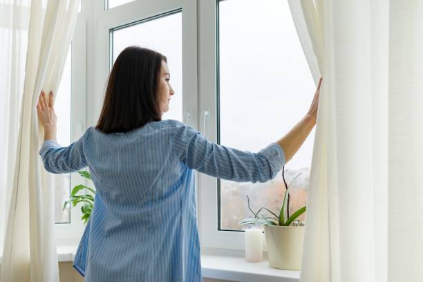 istock Young woman looking out window, cloudy winter day 1214304677