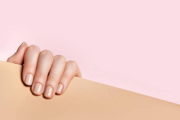 Female hand holds a sheet of paper and demonstrates a nude manicure Female hand holds a sheet of paper and demonstrates a nude manicure. Pink, beige background with place for text. nail polish stock pictures, royalty-free photos & images