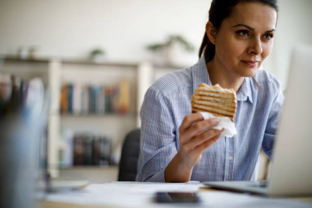 mature woman working from home - eating sandwich emotional stress food imagens e fotografias de stock