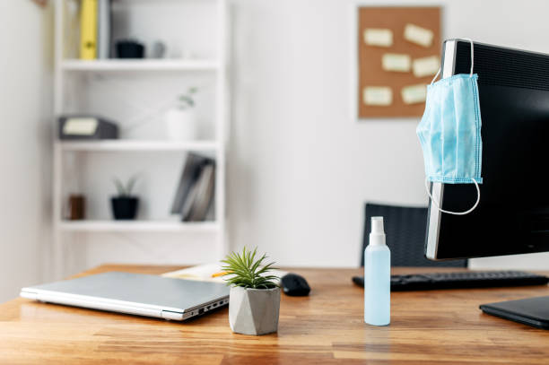 istock Stay at home. Workplace during a pandemic, epidemic. A table with a computer and laptop, a medical mask and an antiseptic, as a measure is careful on it 1214310663