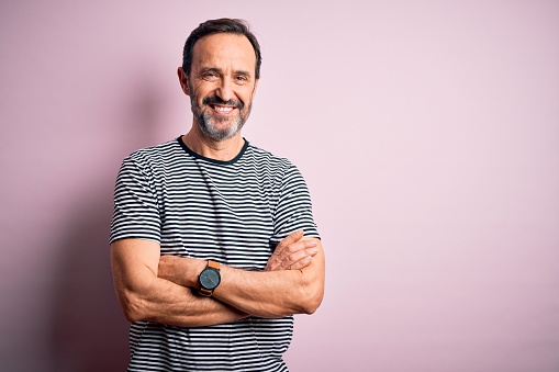 Middle age hoary man wearing casual striped t-shirt standing over isolated pink background happy face smiling with crossed arms looking at the camera. Positive person.