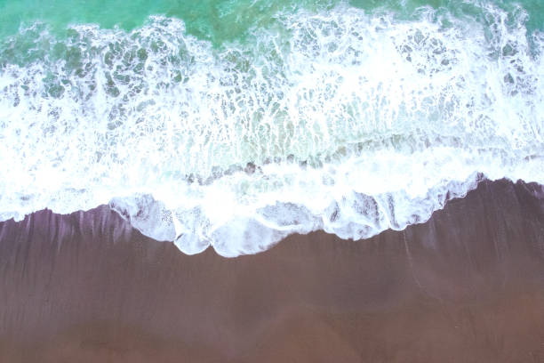 istock Turquoise foaming sea or ocean wave rolls onto a sandy shore. The top view from a height. Light storm in windy weather. Beautiful and calming seascape for wallpaper. Travel and vacation concept. 1214315283