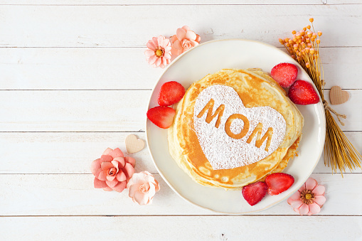Pancakes with heart shape and MOM letters. Mothers Day breakfast concept. Overhead view against a white wood background.