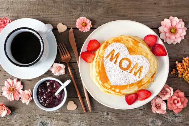Photo of Mothers Day breakfast pancakes with heart shape and MOM letters, overhead view table scene on rustic wood