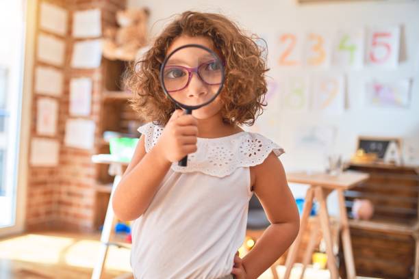 istock Beautiful toddler standing  wearing glasses using loupe at kindergarten 1214319019